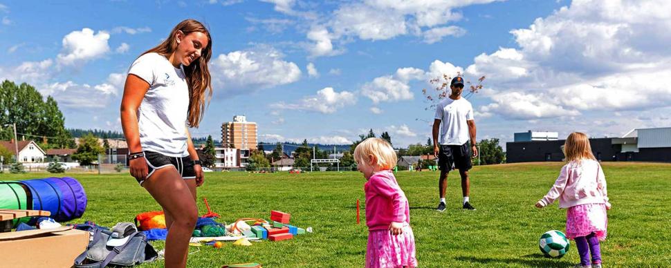 Toddlers and adults playing in a park on a summer day.