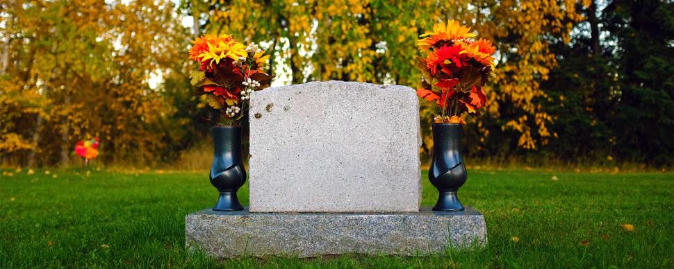 Grave marker flanked by two flower-filled urns in a cemetery.