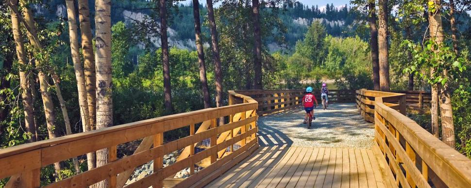 Child and parent on bicycles riding across the bridge at Cottonwood Nature Park.