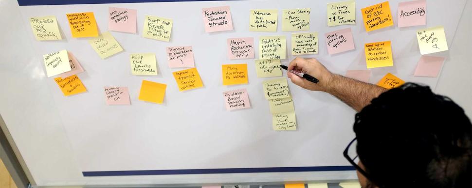 A man placing a sticky note on a whiteboard covered with sticky notes.