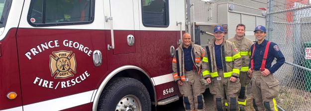 Four firefighters posing alongside a fire truck.