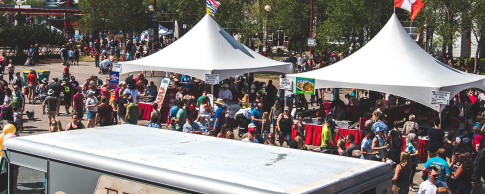 Crowded event in a parking lot, with food trucks and white tents.