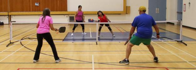 4 people playing pickleball in a school gymnasium. 