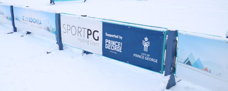 A banner on a snowy field that reads: SportPG Hosting Grant, supported by (Tourism PG logo) and (City of Prince George logo)