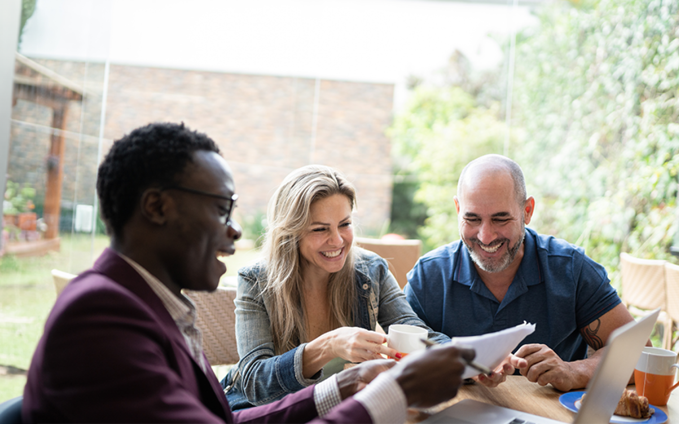 Three people sitting at a table and smiling while looking at documents